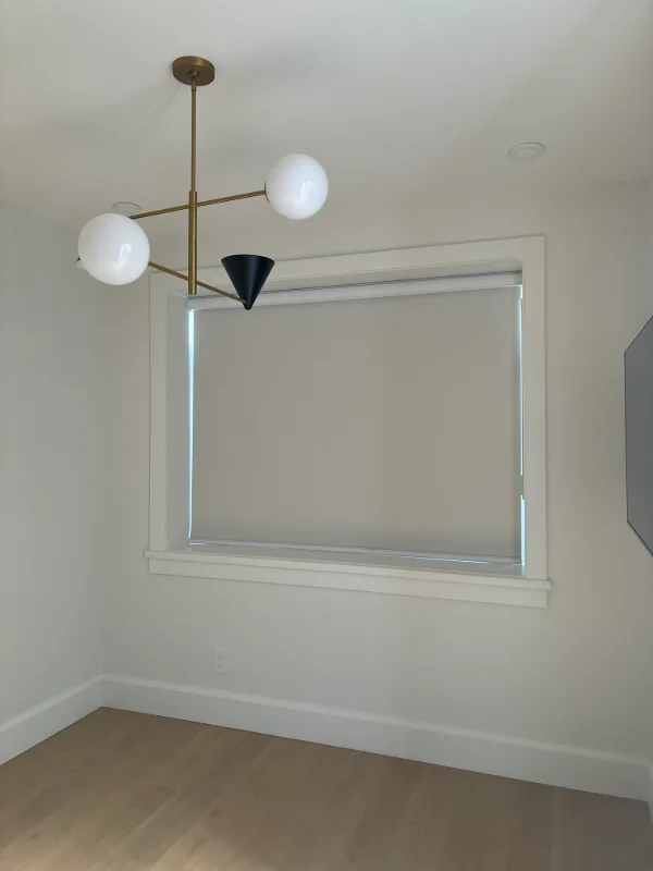 White roller shade in a bright dining room with a brass globe chandelier