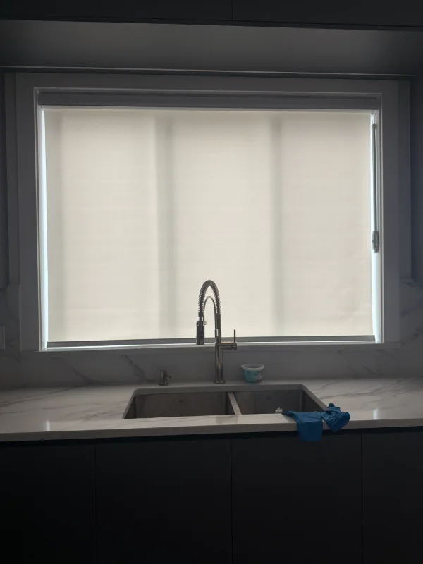 Roller shade over a kitchen sink window with dark cabinets